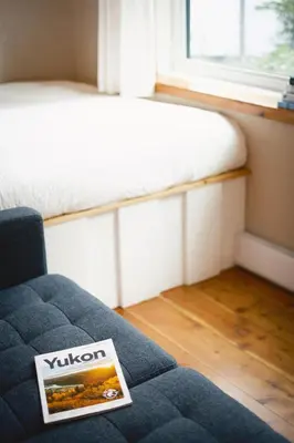 a couch with a book on it in a room with a window at Black Spruce - Yellow Door in Whitehorse
