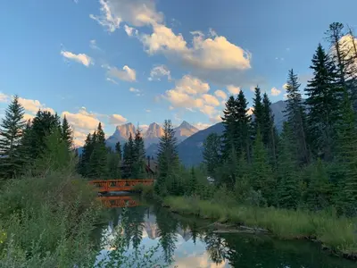 a bridge over a river with trees and mountains at Enchanted Mountain Getaway in Canmore