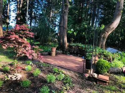 a wooden deck in a garden with trees at Saanichton Waterfront 2BR suite with superb views in Saanichton