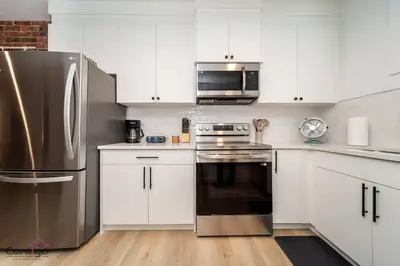 a kitchen with white cabinets and a stainless steel refrigerator at Luxe New York Style Bsmt Suite, Near DT & WEM, King Bed, WiFi in Edmonton