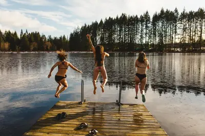 three women jumping off a dock into a lake at Tiny house & Sauna on Lakefront Farm Oasis in Merville