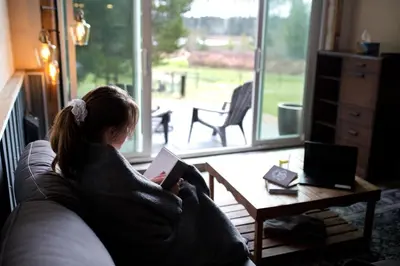 a woman sitting on a couch reading a book at Tiny house & Sauna on Lakefront Farm Oasis in Merville