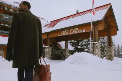 a man walking in the snow in front of a lodge at Post Hotel & Spa in Lake Louise