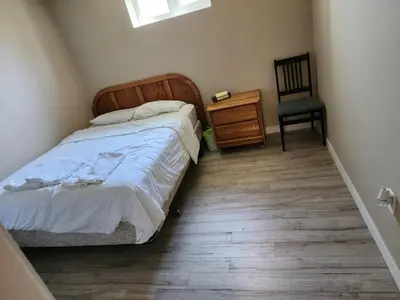 a bedroom with a bed and a chair and a wooden floor at Economical Homestay hostel in Burnaby