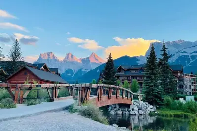 a bridge over a river with mountains in the background at Unit #201 Cozy Mountain View 1BR in DT in Canmore