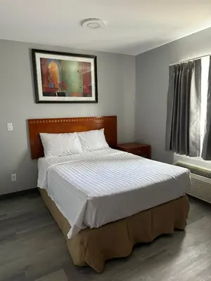 a bedroom with a large bed with white sheets at RAMSHORN MOTEL in Lumby