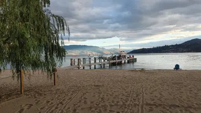 a beach with a pier and a person sitting on the sand at Beds By the Bridge in Kelowna