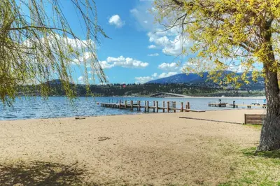 a beach with a tree and a dock at Beds By the Bridge in Kelowna