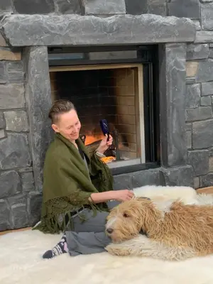 a man sitting next to a dog in front of a fireplace at Romantic Luxury Retreat with Private Sauna & Spa, Pet Friendly, Elkside Hideout B&B in Canmore