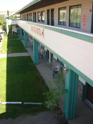 a long building with green columns and a sidewalk at Hoo-Doo Motel in Drumheller