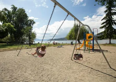 a little girl sitting on a swing at a park at Resort Style Living with Private Lawn and Patio in Kelowna
