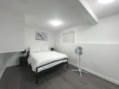 a white bedroom with a bed and a fan at Cozy 3 beds Suite Near Calgary Airport Sleeps 6 in Calgary