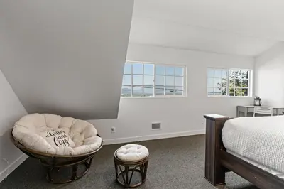 a bedroom with a bed and a chair and two windows at Private Mountainside Home in Chilliwack