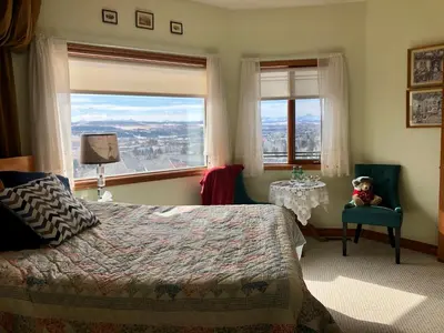 a bedroom with a bed and a chair and a window at Rocky Mountain View Bed & Breakfast in Cochrane