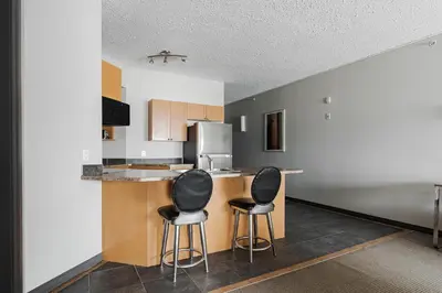 a kitchen with two bar stools and a refrigerator at Premier Residence - Fort McMurray in Fort McMurray