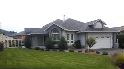 a house with a garage and a green yard at Comfy KING Bed, Large private Basement Suite, Smart TV in Penticton- city of PEACHES AND BEACHES in Penticton