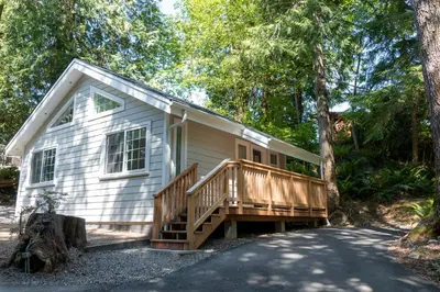 a small white house with a wooden porch at Surfs Inn Guesthouse & Cottages in Ucluelet
