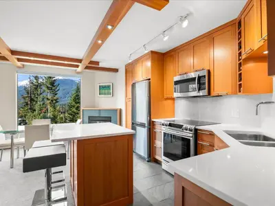 a kitchen with wooden cabinets and a large window at Ski In/Out, Steam Shower, Pool, Hot Tub, Sauna in Whistler