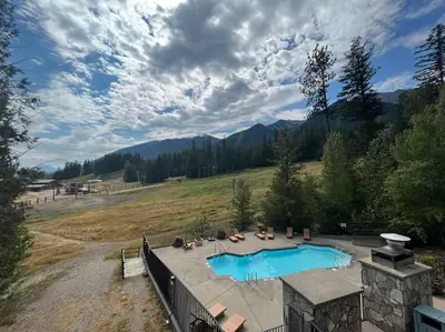 a large swimming pool in a field next to a mountain at Snow Creek Lodge by StayIn in Fernie