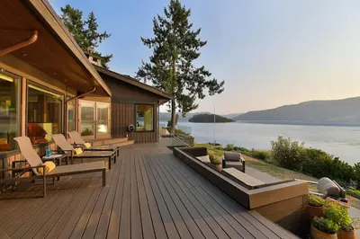 a house with a deck with chairs and a lake at Island Luxury Oceanside Estate by EMR Vacation Rentals in Saanichton