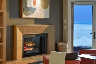 a living room with a fireplace with a view of the ocean at Island Luxury Oceanside Estate by EMR Vacation Rentals in Saanichton