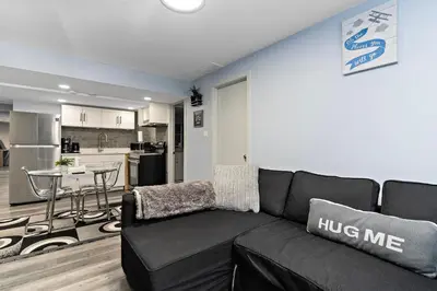 a living room with a black couch and a kitchen at The Cozy Cove - Modern Private Basement Suite with Comfort & Charm, Free Parking, WiFi, Netflix Close to airport & 18 minutes to West Edmonton Mall in Edmonton