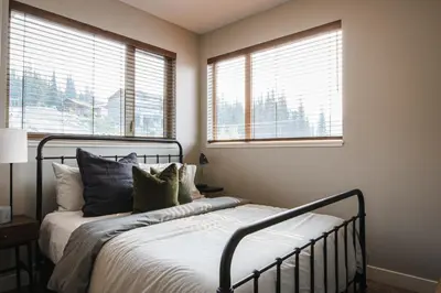 a bedroom with a bed with pillows and two windows at New! Luxury, Top Floor, Ski in/Ski Out, Private Hot Tub and Mountain Views in Sun Peaks