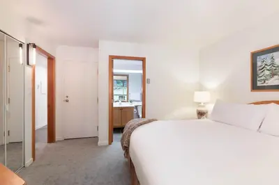 a bedroom with a large white bed and a bathroom at Woodrun Lodge 214 | Ski-in-Ski-Out Condo, Heated Pool, Hot Tub, Gym in Whistler