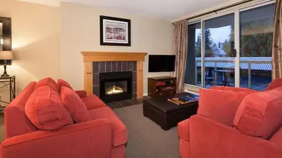 a living room with two red chairs and a fireplace at Woodrun Lodge 211 | Ski-In Ski-Out Condo w/ Heated Pool, Hot Tub, Parking, & Gym in Whistler
