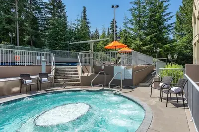 a swimming pool with chairs and an umbrella at Woodrun Lodge 211 | Ski-In Ski-Out Condo w/ Heated Pool, Hot Tub, Parking, & Gym in Whistler