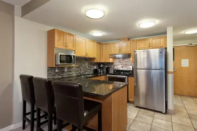 a kitchen with wooden cabinets and a stainless steel refrigerator at Woodrun Lodge 514 | Ski-In Ski-Out Condo w/ Pool, Hot Tub, Free Parking, Wifi & Laundry in Whistler