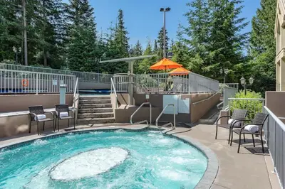 a swimming pool with chairs and an umbrella at Woodrun Lodge 514 | Ski-In Ski-Out Condo w/ Pool, Hot Tub, Free Parking, Wifi & Laundry in Whistler