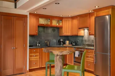 a kitchen with wooden cabinets and a table with green chairs at The Ikon Lofted Studio with King Bed and Patio in Whistler