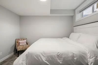 a white bedroom with a bed and a chair at Extra Large House with AC, Banff Access, Sleep 12, BBQ, 4 Bedrooms & 2 Sleeper Sofa Beds in Airdrie
