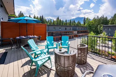 a deck with chairs and a table and an umbrella at Peak Paradise by Revelstoke Vacations in Revelstoke