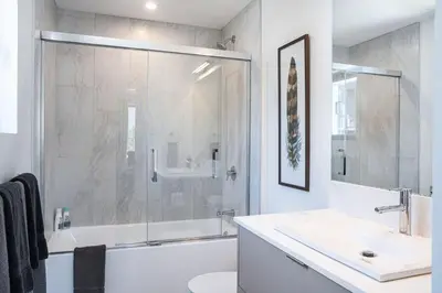 a white bathroom with a shower and a sink at The Stoke Stopover - Revelstoke Condo with Hot Tub in Revelstoke