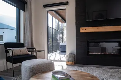 a living room with a fireplace and a chair and a table at Altitude Adjustment by Revelstoke Vacations in Revelstoke