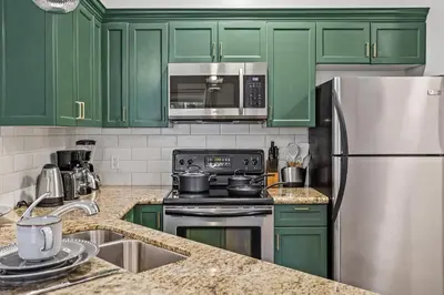 a kitchen with green cabinets and a stainless steel refrigerator at G222 Family Fun- MTN View Stay, Water slide, Pool, Hot Tub, Free Parking in Canmore