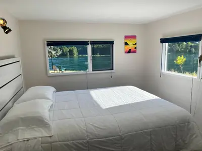 a white bedroom with a bed and two windows at Waterfront, Mountainview House in Castlegar in Castlegar