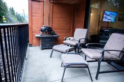 a porch with three chairs and a grill on it at Absolutely Revy - Ground Level Condo in Revelstoke in Revelstoke