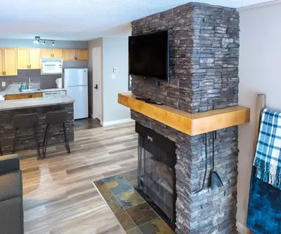 a living room with a stone fireplace with a flat screen tv at 2 Bedroom and Wall Bed Mountain Getaway Ski In Ski Out Condo with Hot Pools Sleeps 8 in Panorama