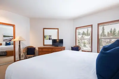 a bedroom with a bed and a tv and two windows at Blackcomb Greens by Outpost Whistler in Whistler