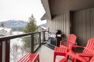 a balcony with two red chairs and a grill at Blackcomb Greens by Outpost Whistler in Whistler