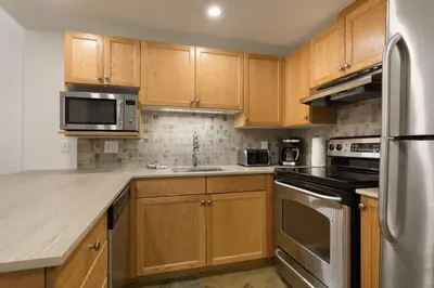 a kitchen with wooden cabinets and stainless steel appliances at Woodrun Lodge 414 | Cozy Ski-In Ski-Out Condo w/ Shared Hot Tub, Pool, Fireplace, & Parking in Whistler