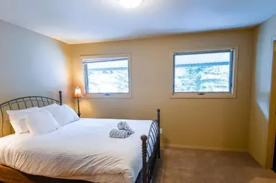 a bedroom with a bed with white sheets and two windows at Thunder Ridge Chalet by Fernie Lodging Company in Fernie