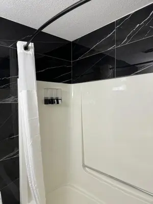 a bathroom with a white shower curtain and black tiles at The Viking Inn in Viking