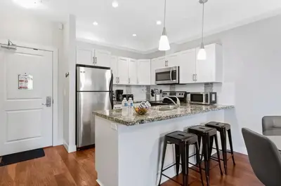 a kitchen with white cabinets and a counter with bar stools at Kelowna family-friendly lake & Mountain view Luxury condo with AC, pool, Hot tub, near winery and shopping center in West Kelowna
