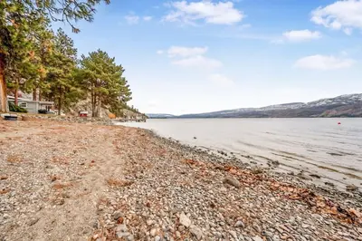 a rocky shore of a lake with houses and trees at Cozy Cottage by the Lakeshore #4 in West Kelowna