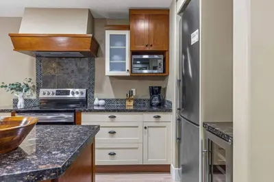 a kitchen with white cabinets and a stainless steel refrigerator at Gorgeous Mountain Condo - Hot Tub & Pool managed by Little Sister Getaways in Canmore