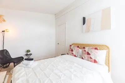 a white bedroom with a bed with a black chair at Beautiful Vancouver Special Home in Vancouver
